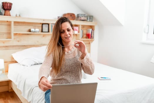 Woman vediocalling through laptop from bedroom with wired headphones