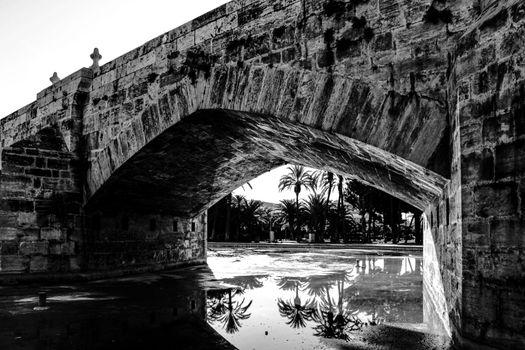 Old Stone bridge and reflections in a park puddle in Valencia