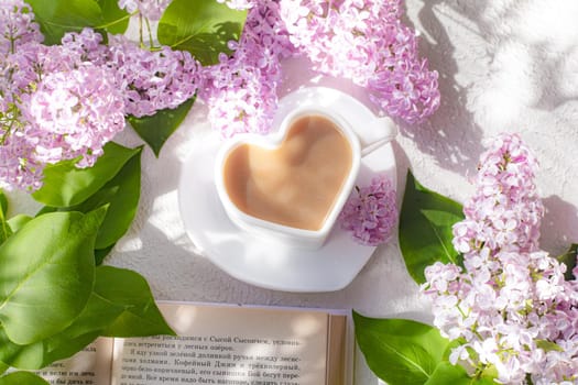 Cappuccino coffee in a cup with a book and a branch of lilac on a white background with shadows . A hot drink. Reading books. relax. Cafeteria advertising concept. Article about cappuccino. Making cappuccino. Lilac branches. Spring. Copy space