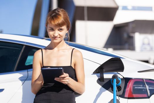 Girl working on tablet while her electric car is charging.