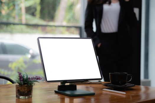 Mockup digital tablet on wooden desk with blank screen. Business people working at background