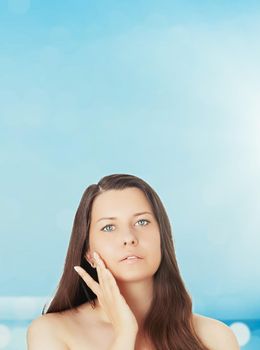 Skincare and sun protection in summer. Portrait of a beautiful young suntanned woman, blue sea and sky on background, beauty, wellness and travel concept.