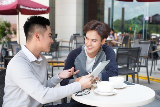 Two young handsome businessmen with tablet discussing project