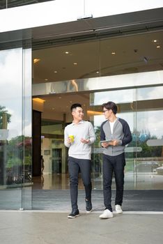 Two asian men talk and use smart phone outside the building