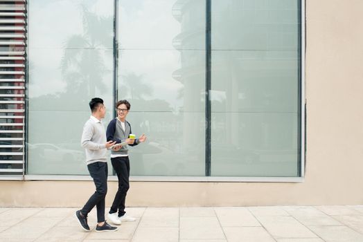 Two asian men talk and use smart phone outside the building