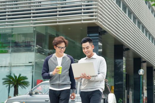 Two smiling young businessmen walking and talking in the city