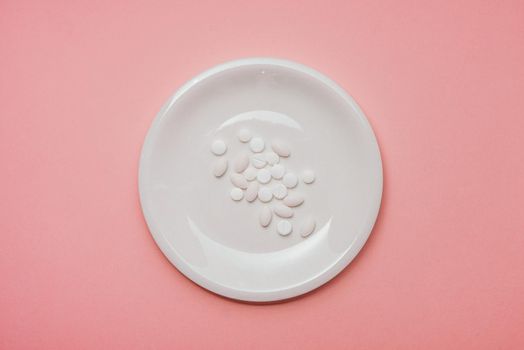 Pills served as a healthy meal. Drug capsule on white plate on pink background