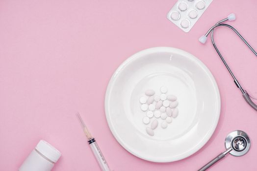 Pills served as a healthy meal. Drug capsule on white plate on pink background