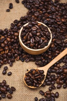 Wooden bowl with roasted coffee beans on rustic background.