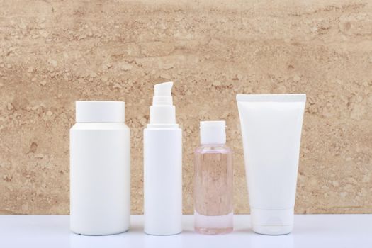 Set of beauty products for daily skin care in white unbranded tubes on white bathroom shelf against beige marble background. Concept of cosmetic products for skin cleaning, exfoliating, hydrating and anti age treatment