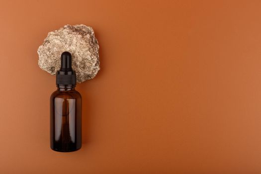 Skin serum in dark glass bottle on natural stone against brown background with copy space. Concept of cosmetics for african american skin 