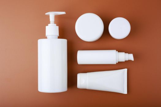 Top view of wide set of beauty products for daily skin care routine in white unbranded containers on brown background. Concept of skin care routine for african american skin