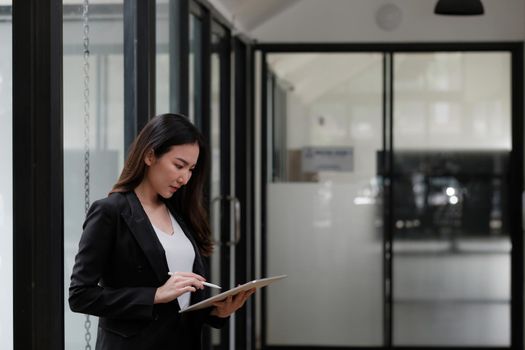 Asian businesswoman holding stylus pen writing on digital tablet at meeting table.