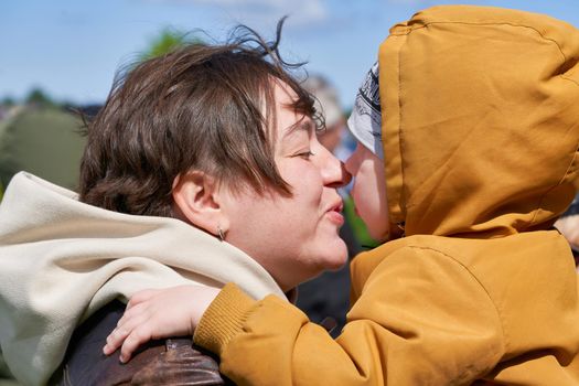 Mom with short hair kisses her little son while holding him in her arms. Family values