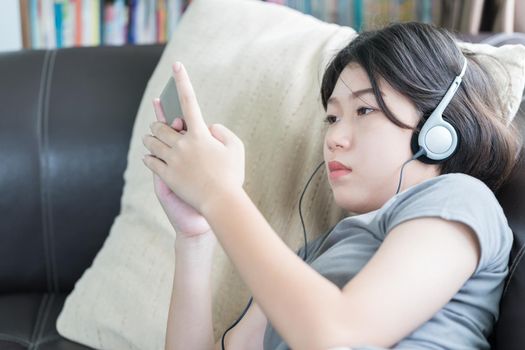 Close up young asian woman short hair listening music from mobile phone on the couch at home