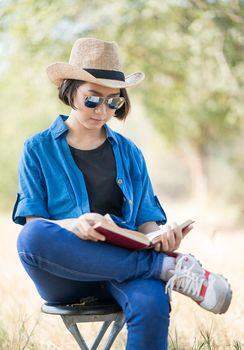 Young asian women short hair wear hat and sunglasses read a book ,sit on chair in countryside Thailand