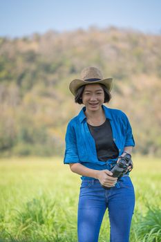 Young asian woman short hair wear hat and hold binocular in grass field countryside Thailand