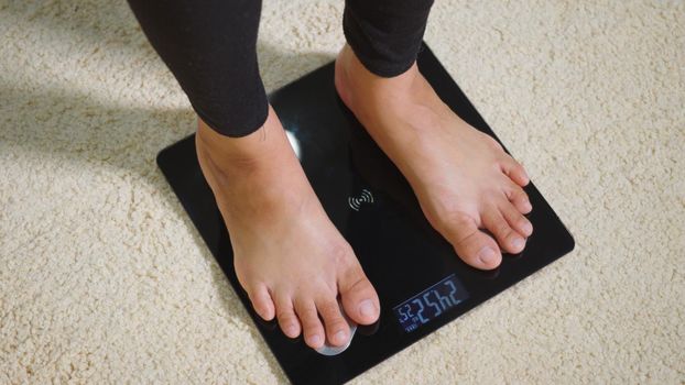 Asian young woman leg stepping standing on floor electric scales, female working out at home in living room, female stand on digital weighing machine. Healthy weight loss control concept, slow motion