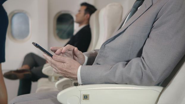 Happy businessman using wifi texting or playing mobile phone sitting in airplane he's toughing smartphone screen, internet for reading news device during flight, business travel concept