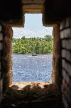 Observation window in the brick wall of the fortress for firing a gun with a view of the river water and the forest