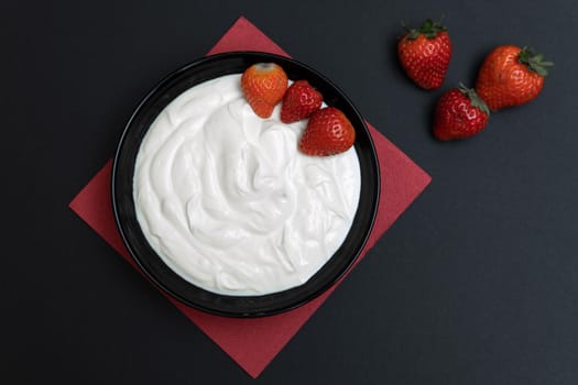 Plain yogurt with strawberries, red napkin and black background