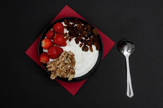 Plain yogurt with strawberries, red napkin, spoon and black background