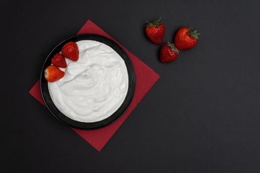 Plain yogurt with strawberries, red napkin and black background