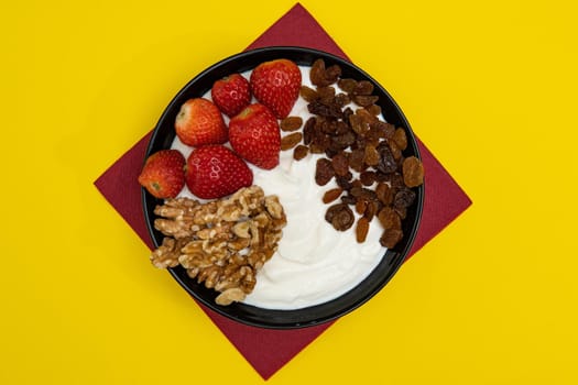 Plain yogurt with strawberries, red napkin, raisins, walnuts and yellow background