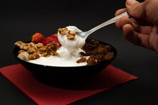 Plain yogurt with strawberries, red napkin, raisins, walnuts, spoon and black background