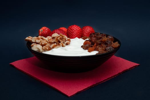 Plain yogurt with strawberries, red napkin, raisins, walnuts and black background