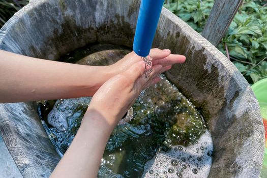 Woman washing her hands with water outdoor at a public faucet