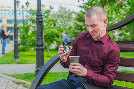 An office worker on a park bench opened a glass of coffee and was unpleasantly surprised at its quality, expressing disgust on his face