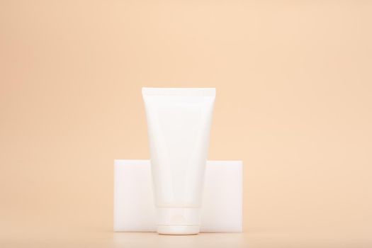Hands or face cream in white glossy tube against light beige background. Concept of organic moisturizing beauty products for face, neck or hands