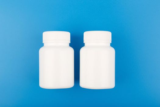 Two white plastic bottles of medicine on blue background. Concept of medical treatment of different diseases