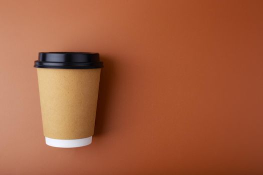 Cardboard cup with tea or coffee on brown background with copy space. Concept of hot drinks for take away