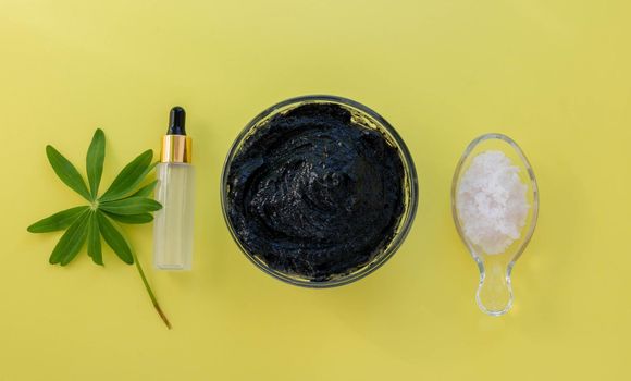 Image of the ingredients of home cosmetics. Black mask, black dirt, pink salt, a bottle with an eyedropper on a yellow background.Skin Care Concept.
