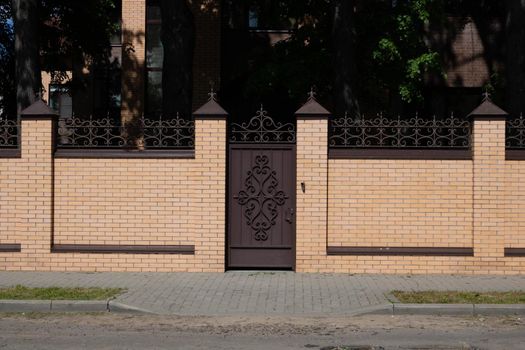 Light brown brick fence and wrought iron door next to the road.
