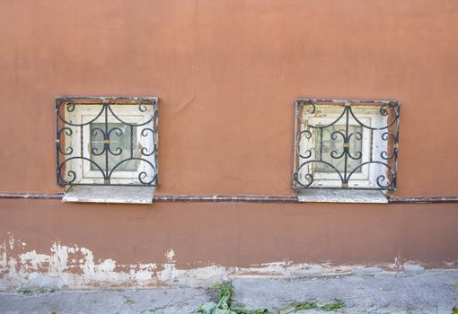 Two windows with antique bars on the plinth .Red facade with small windows.