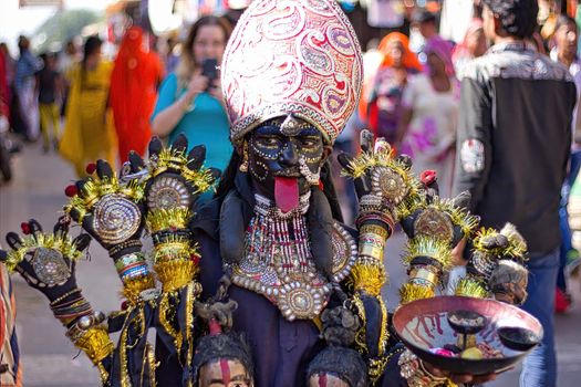 Pushkar, India - November 10, 2016: A young little girl dressed up or disguised as Indian goddess of destruction named maa Kali with crown and multiple hands as street performer during Pushkar fair
