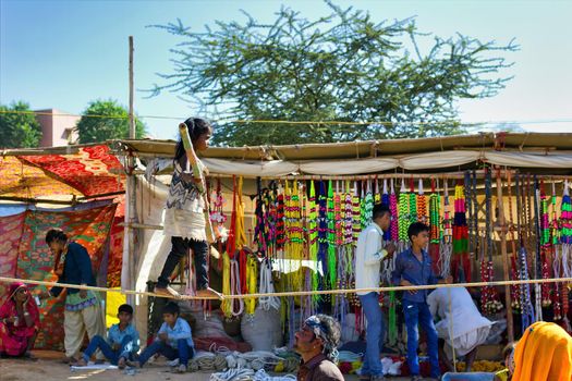 Pushkar, India - November 10, 2016: A little gypsy Indian girl doing show of walking bare foot on a rope performing acrobatic balancing act while holding bamboo stick in her hand during pushkar fair