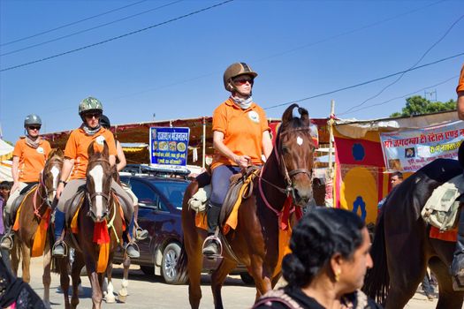 Pushkar, India - November 10, 2016: foreigner tourists riding horses with helmet in the biggest fair of Pushkar in the state of Rajasthan
