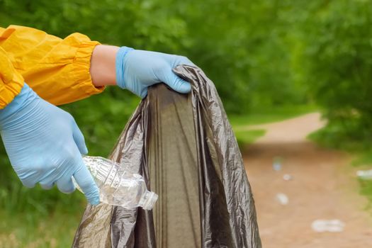 Volunteer hands picks up plastic garbage from grass in park. Volunteer cleaning up trash a forest. Male collects garbage people volunteer work green thinking about nature cleanup forest. Plastic waste