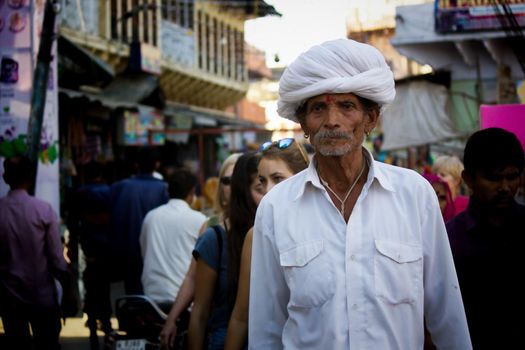 Pushkar, India - November 10, 2016: An old Rajasthani man in traditional ethnic wear such as white turban and typical white kurta walking in a street during pushkar fair in the state of Rajasthan