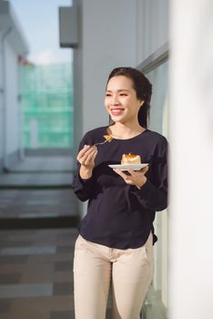 Young happy woman stands on the terrace of the hotel with dish cake in the morning. Pretty asian girl in good mood and is ready for adventures.
