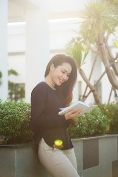 Happy young woman holding book fond of literature analyzing novel during leisure time on terrace of campus cafe in sunny day.