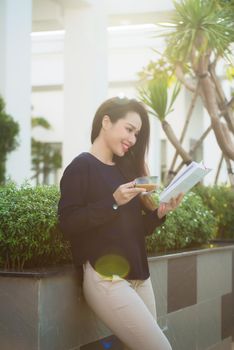 Happy young woman holding book fond of literature analyzing novel during leisure time on terrace of campus cafe in sunny day.