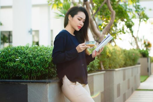 Happy young woman holding book fond of literature analyzing novel during leisure time on terrace of campus cafe in sunny day.