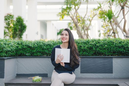 Happy young woman in park on sunny summer day reading book. Cheerful beautiful girl on beautiful day.