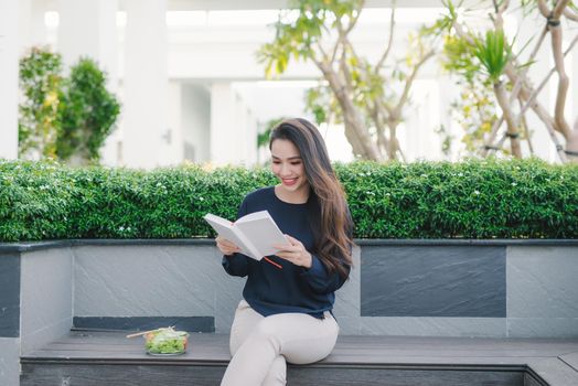 Happy young woman in park on sunny summer day reading book. Cheerful beautiful girl on beautiful day.