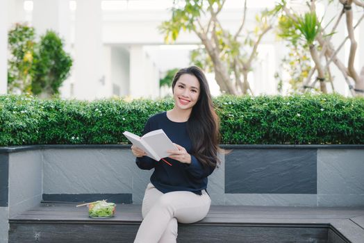 Happy young woman in park on sunny summer day reading book. Cheerful beautiful girl on beautiful day.